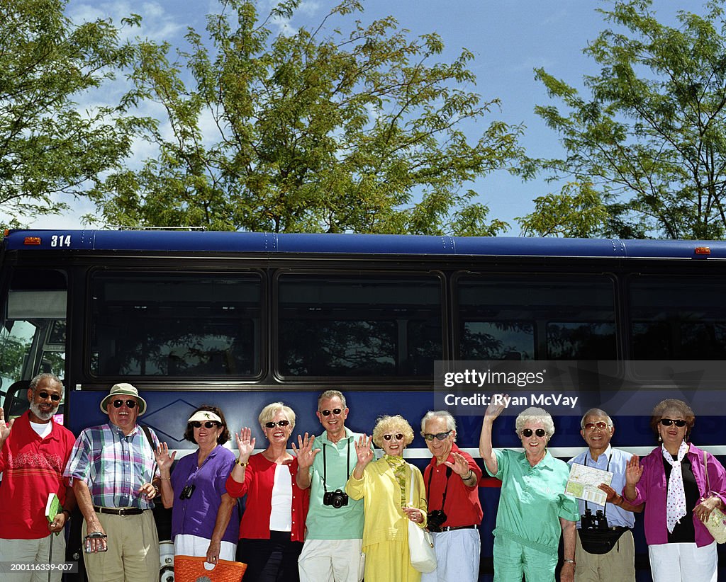 Group of mature adults standing beside charter bus, smiling, portrait