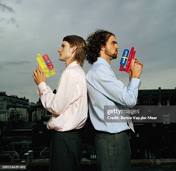 two businessmen back to back holding water pistols, profile - waterpistool stockfoto's en -beelden