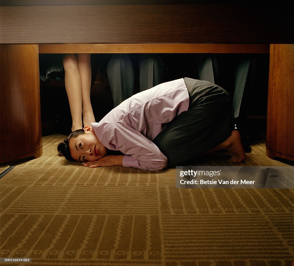 Young woman curled up under table at colleagues' feet