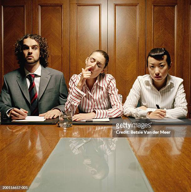 three executives at desk, young woman in centre picking nose - picarse la nariz fotografías e imágenes de stock