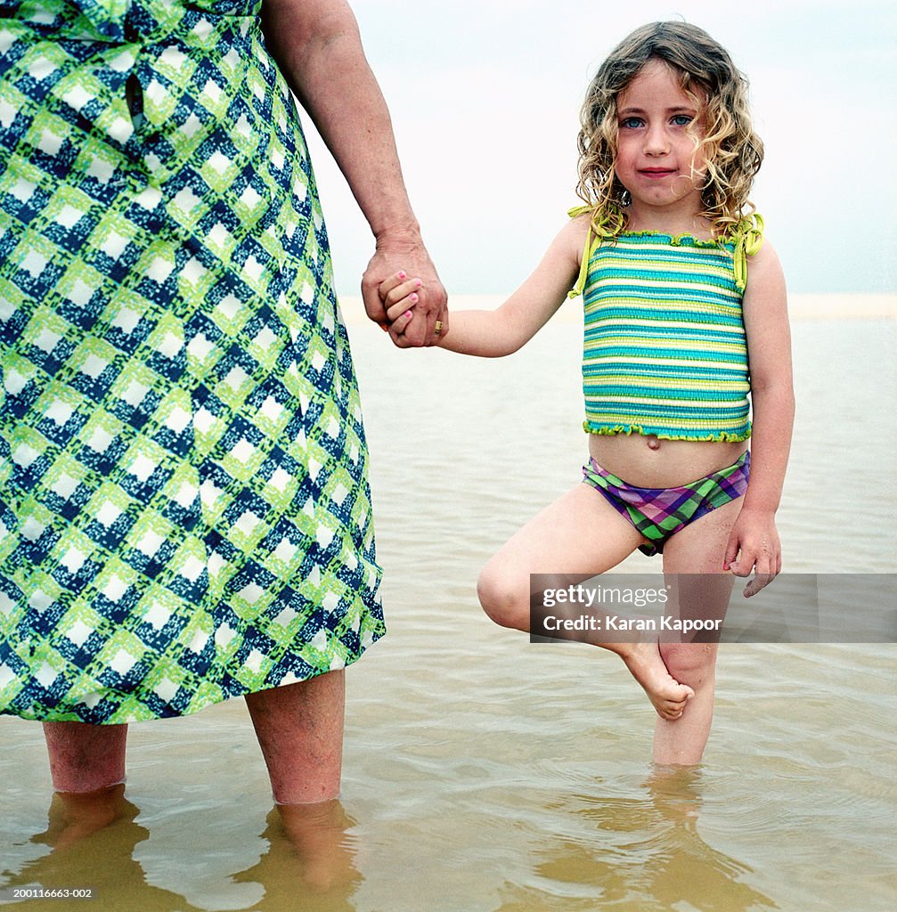 Girl (2-4) holding mature woman's hand on beach, portrait