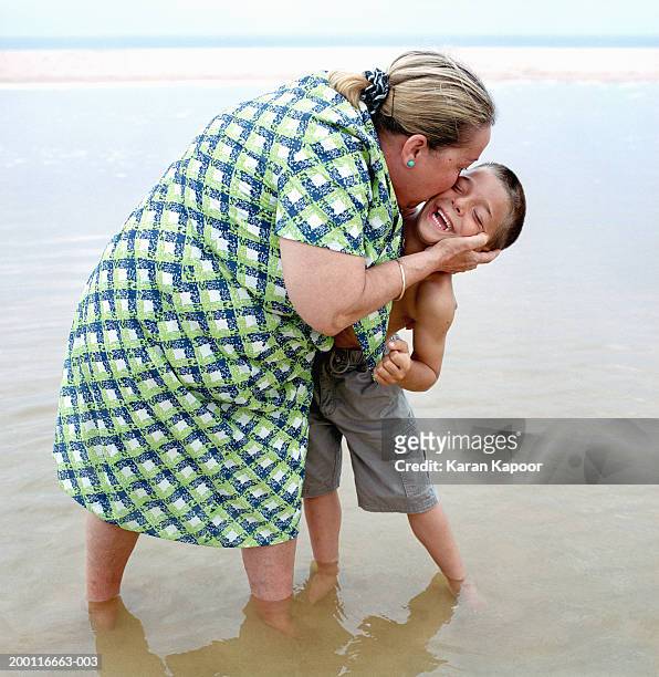 mature woman and boy (5-7) on beach, woman kissing boy on cheek - chubby granny foto e immagini stock