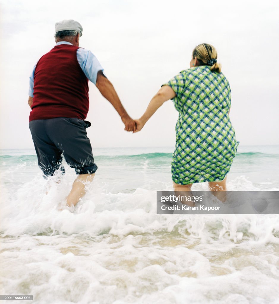 Mature couple playing in surf, rear view