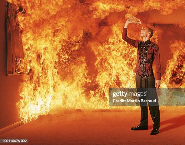 young man pouring water over head in burning room (digital composite) - achtlos stock-fotos und bilder