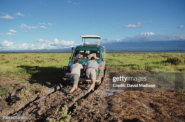 two men pushing vehicle out of mud, rear view - pushing fotografías e imágenes de stock