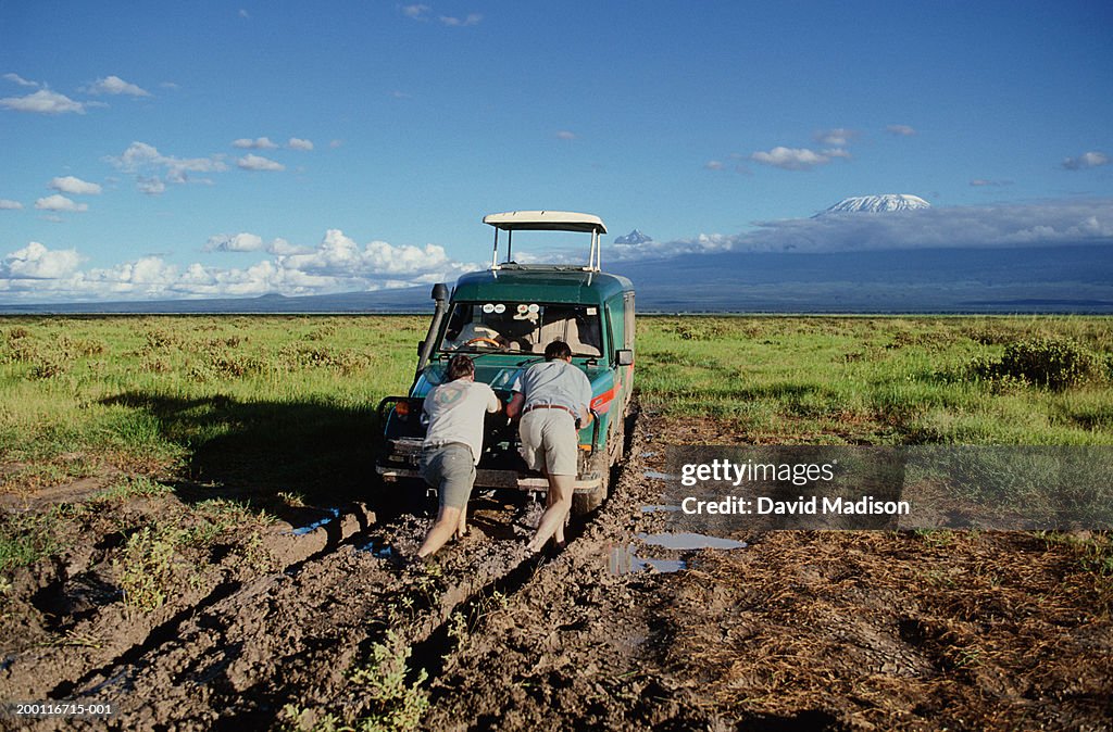 Two men pushing vehicle out of mud, rear view
