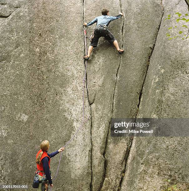 woman holding rope, looking upward at partner climbing rock wall - rock face fotografías e imágenes de stock