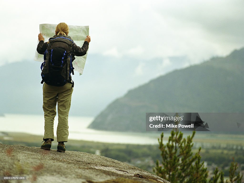 Female backpacker holding map on rock, rear view