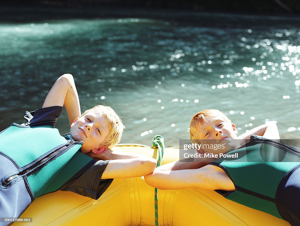 Two boys (8-10) wearing wetsuits, resting on yellow raft, portrait