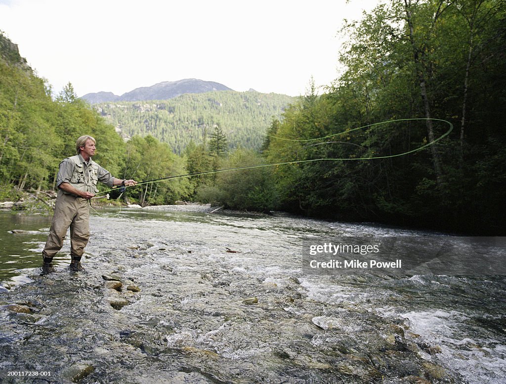 Mature man fly fishing in river, casting line