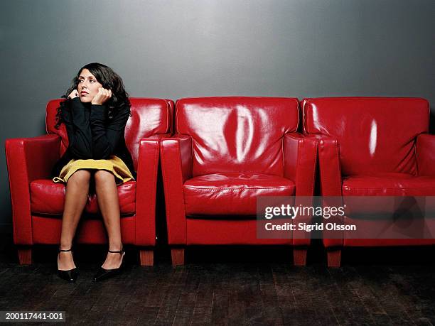 young woman in armchair, hands on chin - rode rok stockfoto's en -beelden