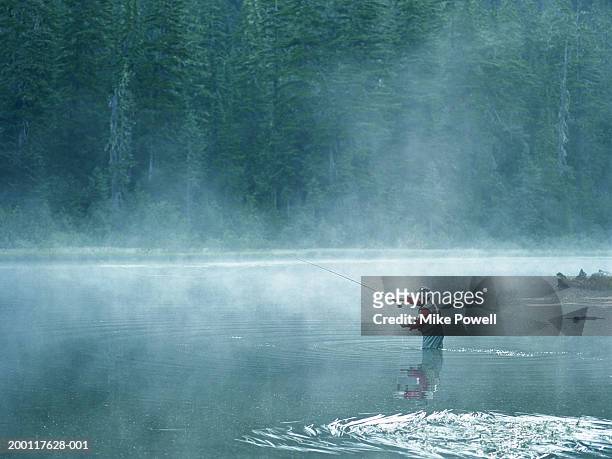 senior fly fisherman standing in lake covered with fog, casting line - fischen stock-fotos und bilder