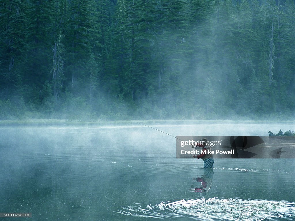 Senior fly fisherman standing in lake covered with fog, casting line