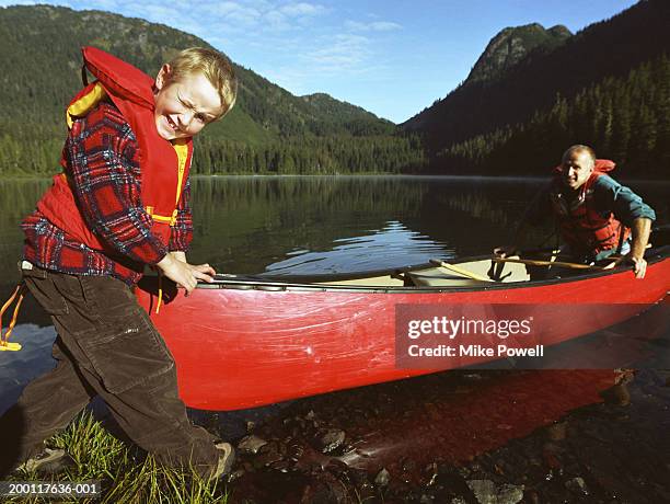 boy (7-9) pushing canoe in to lake with father, portrait - family red canoe stock pictures, royalty-free photos & images