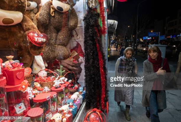 Two Iranian women are walking past a shop window decorated with Valentine's Day gifts in downtown Tehran at night on February 13, 2024.