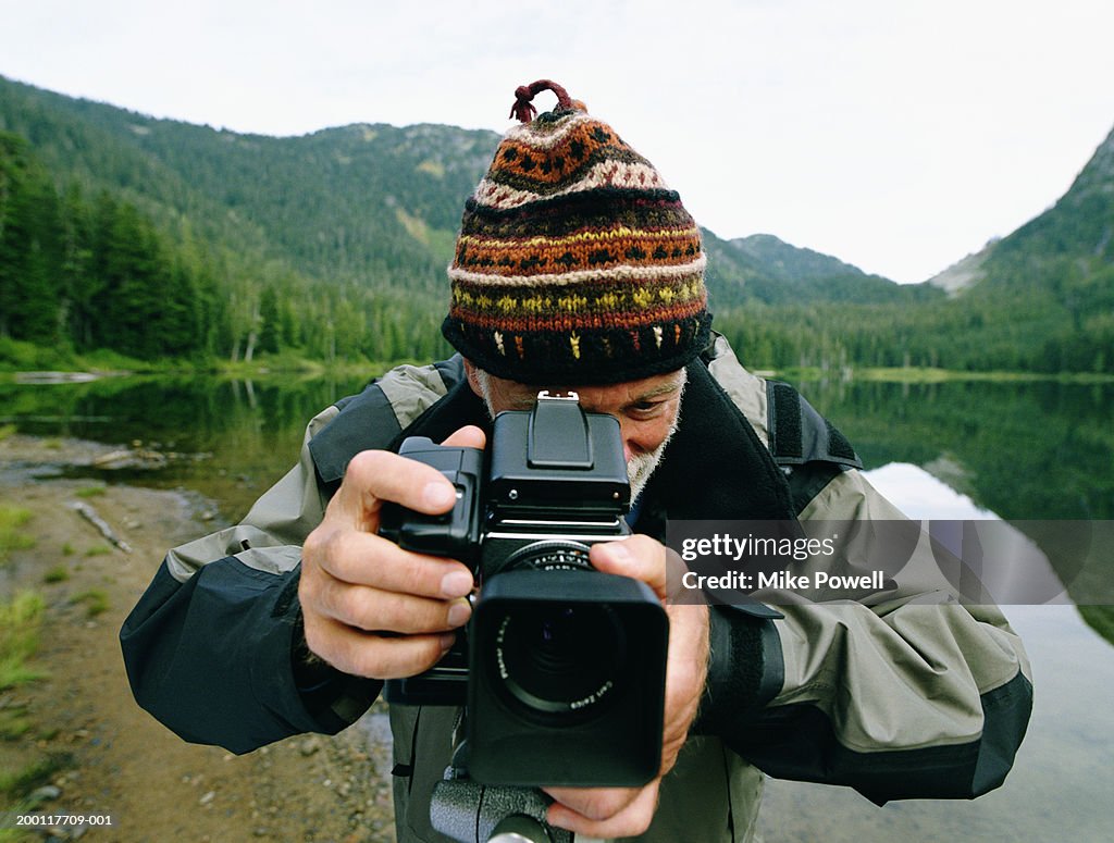 Senior man standing by lake, taking photo with medium format camera