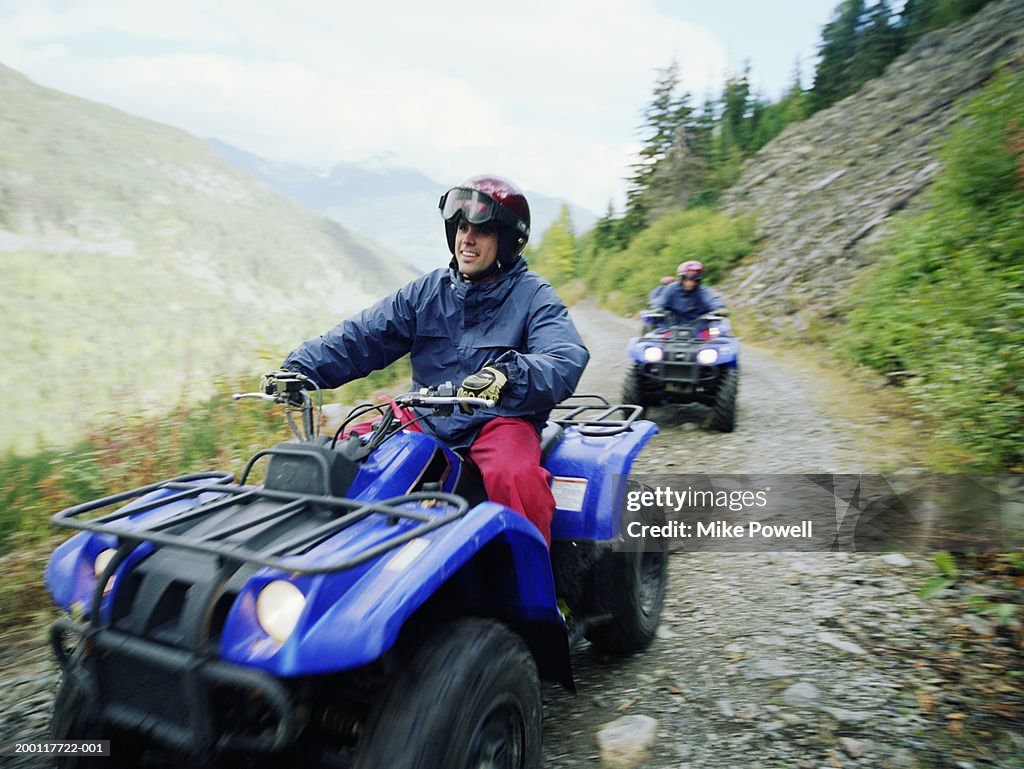 Man driving ATV with group on mountain road, (focus on man)