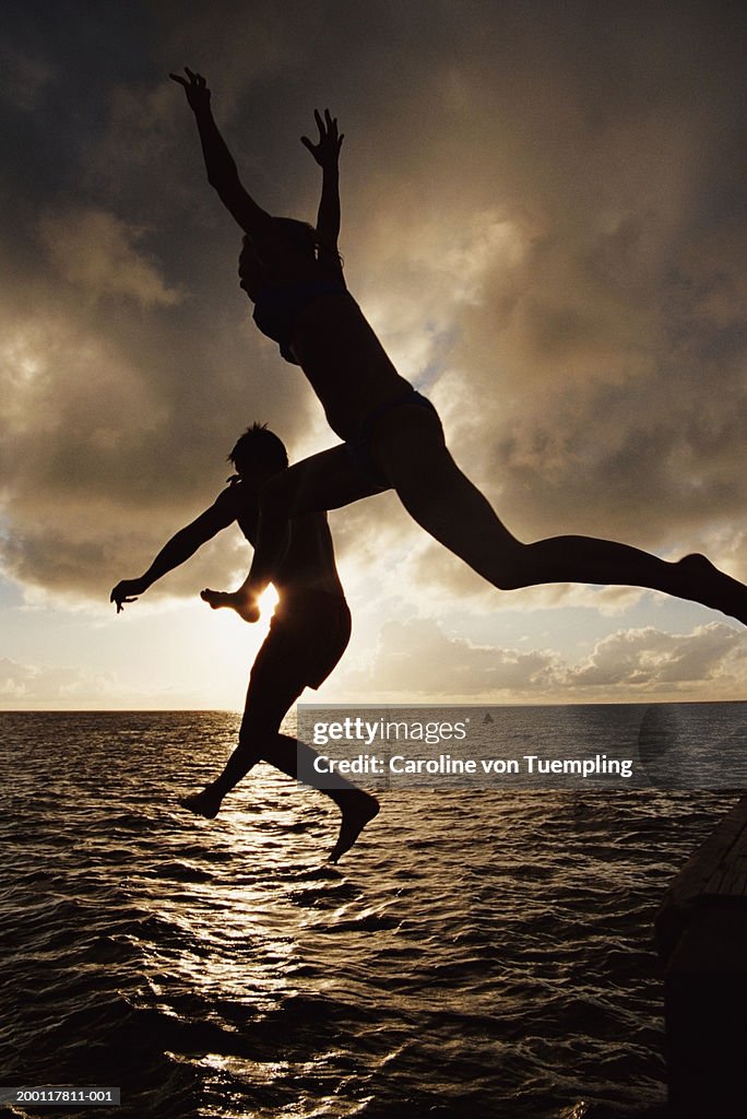 Silhouette of couple jumping into ocean