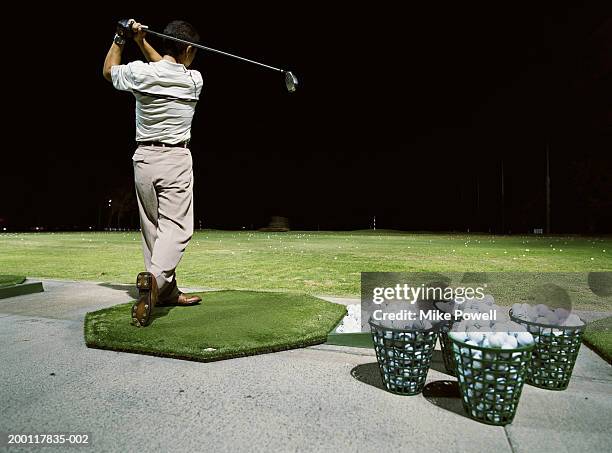 man practicing golf on driving range at night, rear view - swing night stock pictures, royalty-free photos & images