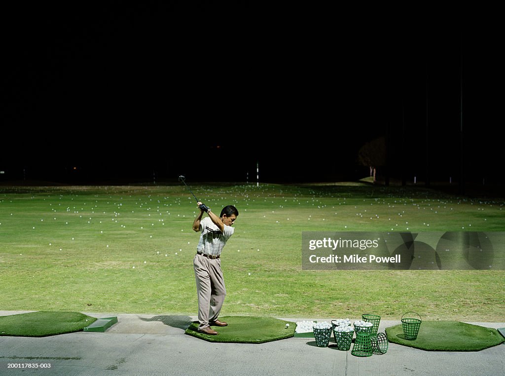 Man practicing golf on driving range at night