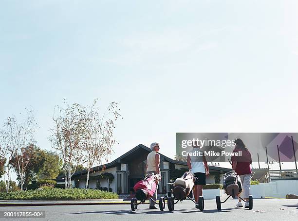 three mature women wheeling golf bags towards club house, rear view - country club photos et images de collection