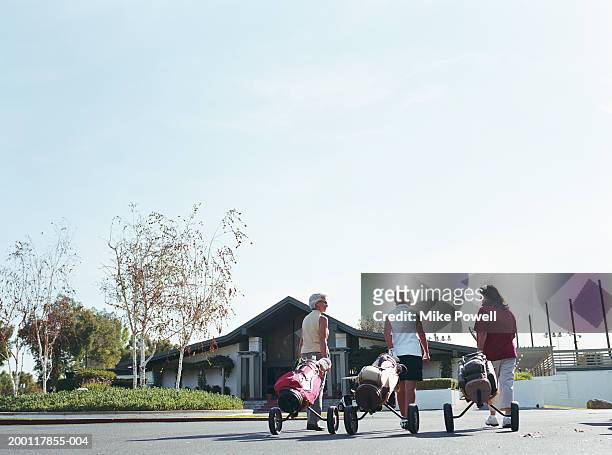 three mature women wheeling golf bags towards club house, rear view - golf clubhouse stockfoto's en -beelden