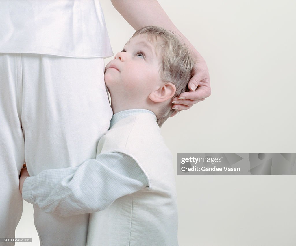 Boy (3-5) hugging mother's leg, looking up