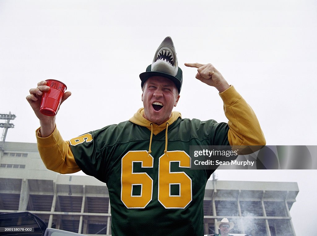 Man pointing at cap with shark design at stadium parking lot