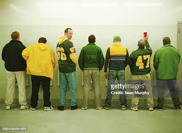 men lined up at urinal, one looking back - urine photos et images de collection
