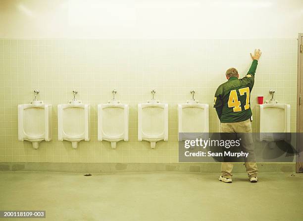 man using urinal, one hand up on tile wall - people peeing stockfoto's en -beelden