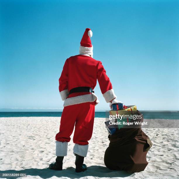 father christmas on beach with sack of presents, rear view - santa leaning stock pictures, royalty-free photos & images