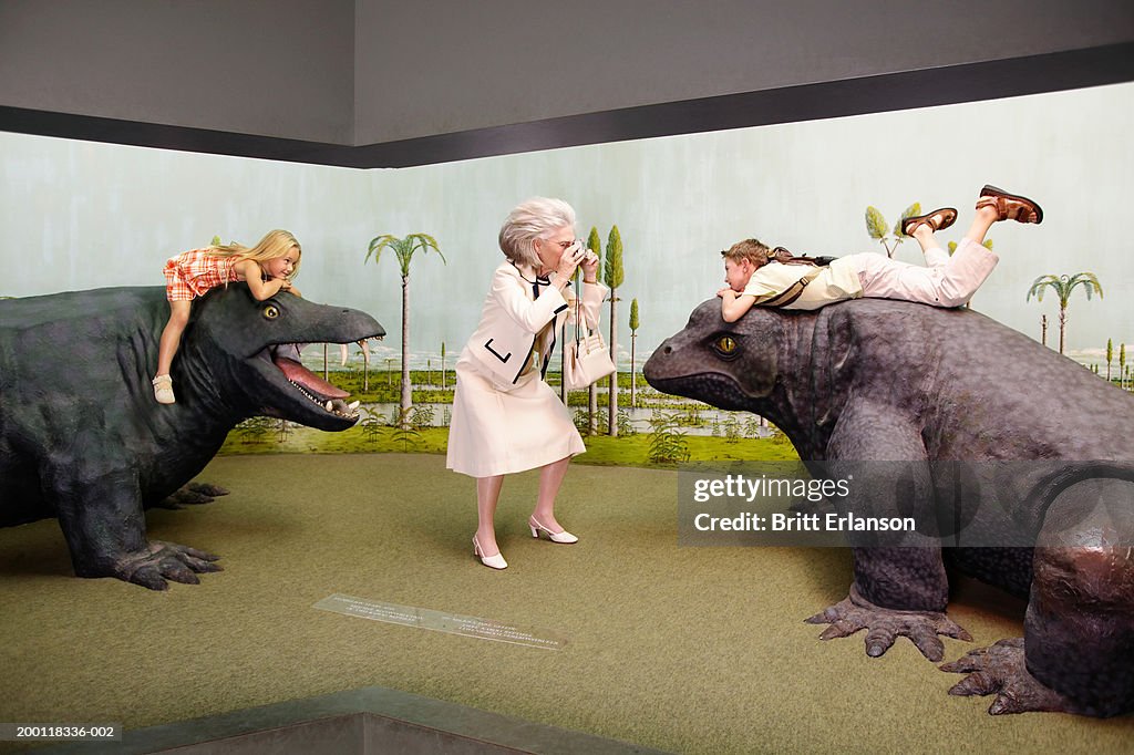 Grandmother taking photo of boy (8-10) on model of prehistoric lizard