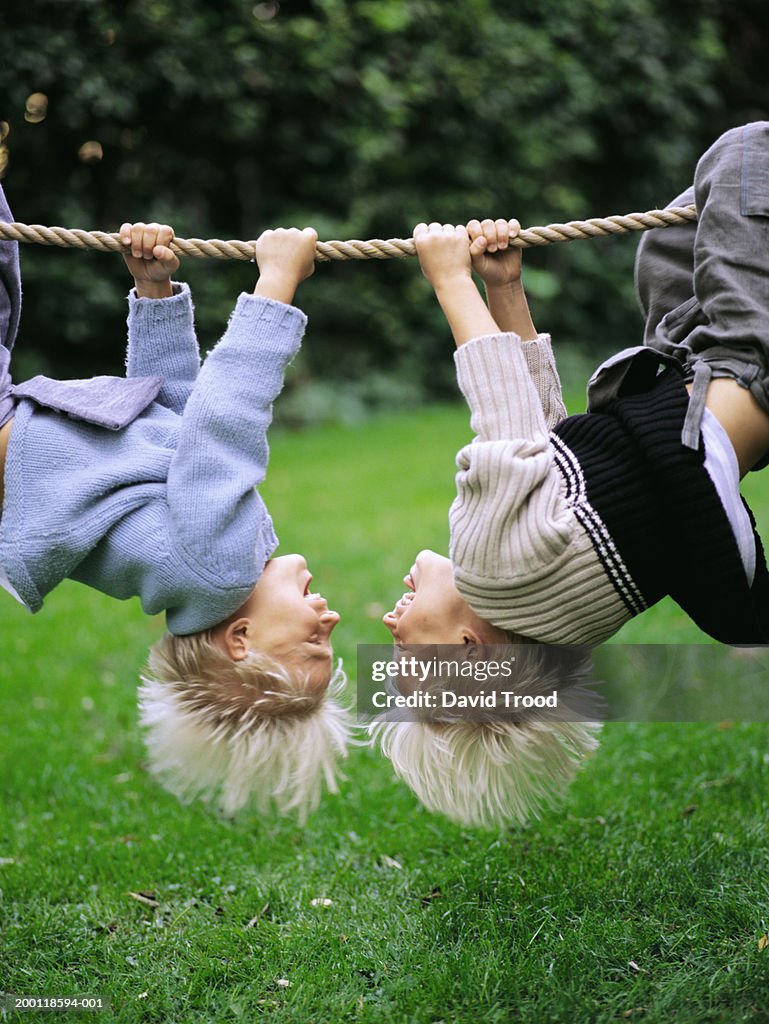 Twin brothers (6-8) hanging from rope, upside down, outdoors