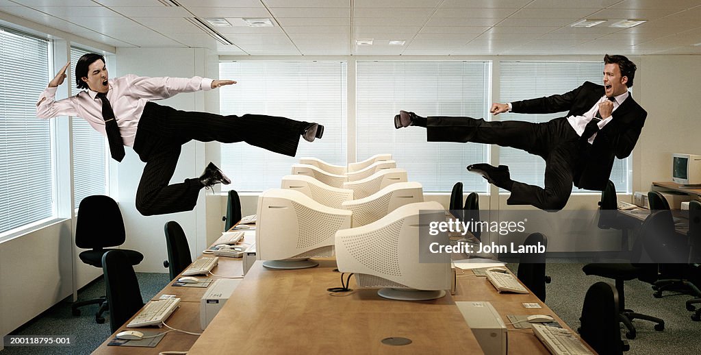 Two men kicking in mid-air across row of computers (Digital Composite)