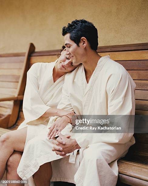 couple sitting on bench in white robes - accappatoio foto e immagini stock