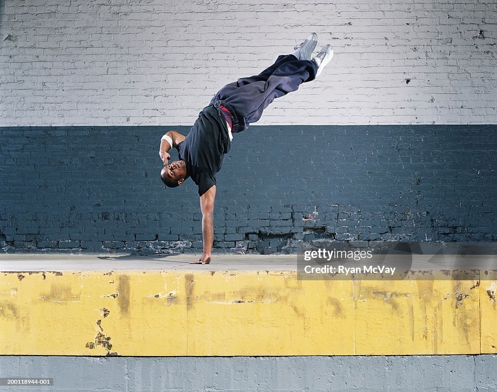 Young man breakdancing on loading dock, balancing on one hand