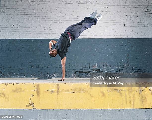 young man breakdancing on loading dock, balancing on one hand - breaking foto e immagini stock