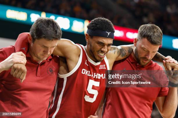 Oklahoma Sooners guard Rivaldo Soares leaves the court with the help of two coaches after hurting his ankle during the Big 12 college basketball game...