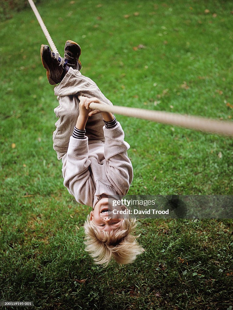 Boy (4-6) hanging upside down on rope, portrait