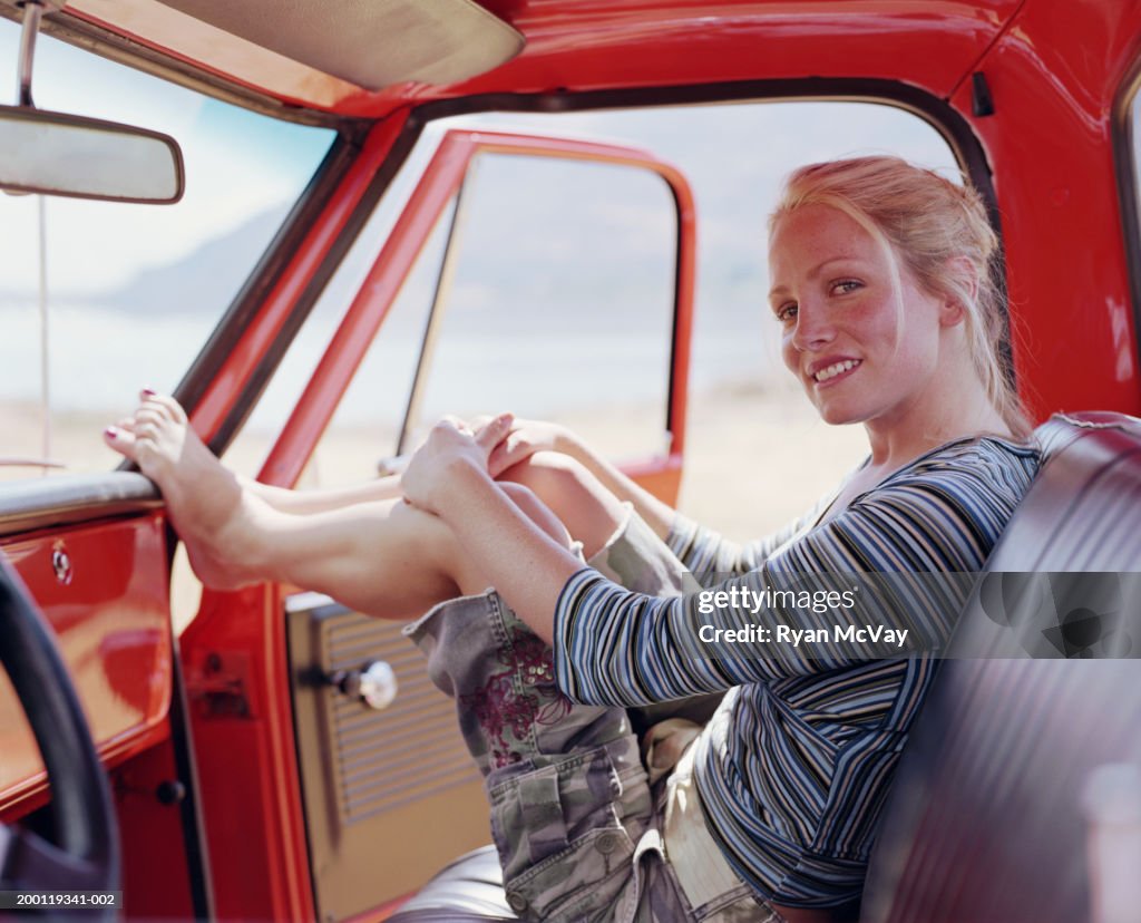 Woman sitting in pick-up truck, resting feet on dashboard, portrait