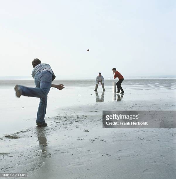 three men playing cricket on beach - beach cricket stock pictures, royalty-free photos & images