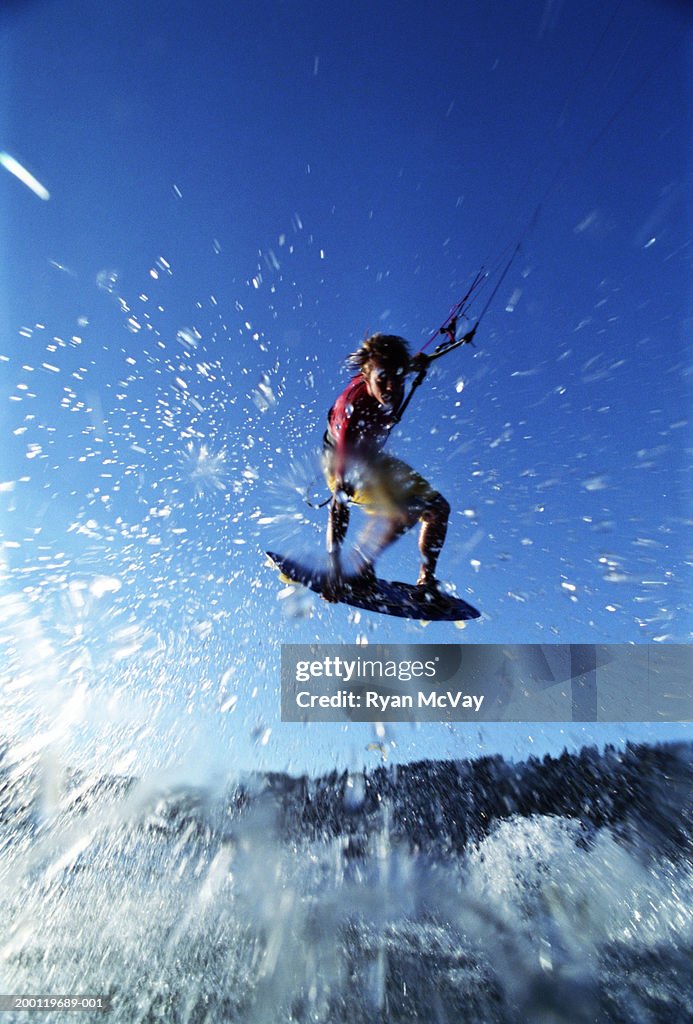 Young male kiteboarder in mid-air, low angle view (blurred motion)