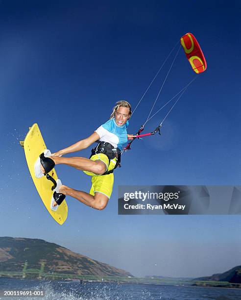 young female kiteboarder grabbing board in mid-air, low angle view - kite surfing stock pictures, royalty-free photos & images