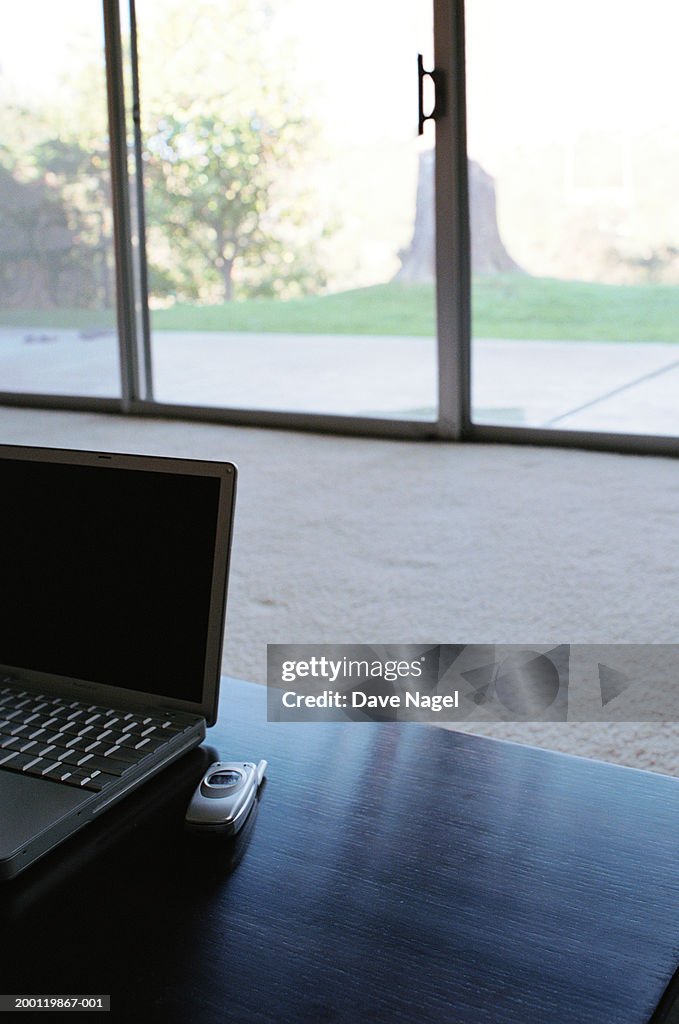 Laptop and mobile phone on table in room (focus on foreground)