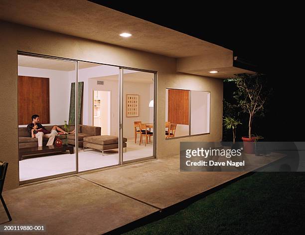young couple relaxing on sofa, view sliding glass doors, night - patio lights stock-fotos und bilder