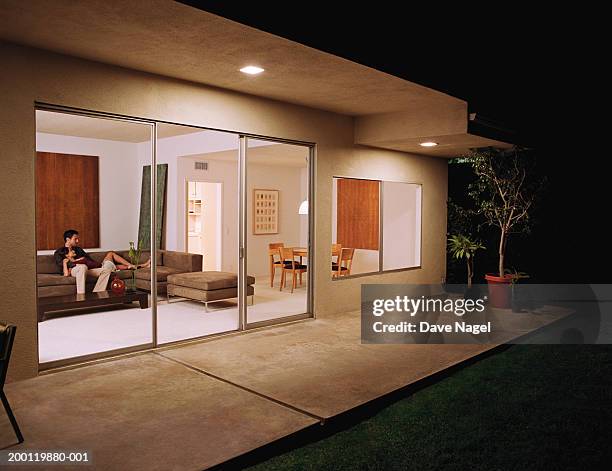 young couple relaxing on sofa, view sliding glass doors, night - sliding door photos et images de collection