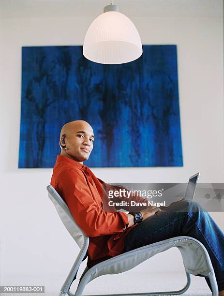 young man wearing headset, using laptop, portrait - mann sitzt auf stuhl stock-fotos und bilder
