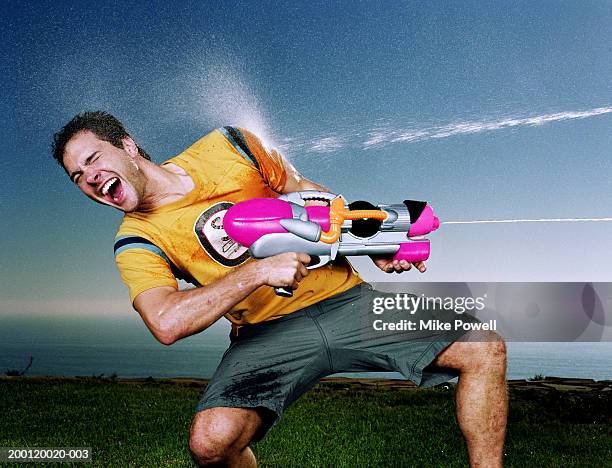 young man with water gun being hit with water blast on arm - waterpistool stockfoto's en -beelden