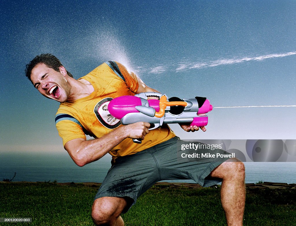 Young man with water gun being hit with water blast  on arm