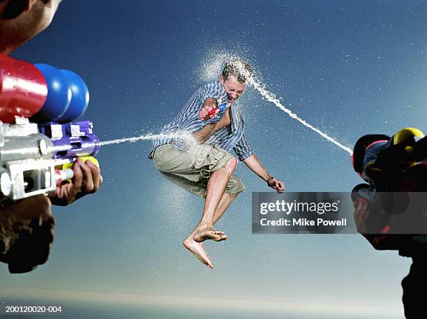 young man being hit with water blast from two water guns - pistola de agua fotografías e imágenes de stock